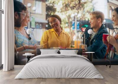 Diverse Group of Friends Enjoying Leisure Time in a Street Cafe. Young Women and Men Sitting Behind a Table, Having Fun and Joyful Conversations. Black African Girl Sharing Motivational Work Stories Wall mural