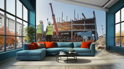 Diverse Team of Specialists Inspect Commercial, Industrial Building Construction Site. Real Estate Project with Civil Engineer, Investor and Worker. In the Background Crane, Skyscraper Formwork Frames Wall mural