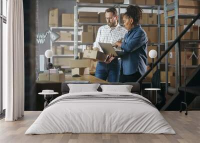 European Male and African Female Working in a Warehouse. Talking, Using Laptop Computer, Checking Retail Stock, Preparing Shipment. Rows of Shelves Full of Cardboard Box Parcels in the Background. Wall mural