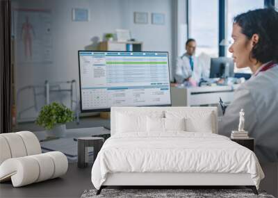 Experienced Female Medical Doctor Wearing White Coat Working on Personal Computer in a Health Clinic. Medical Health Care Professional Working with Test Results, Patient Treatment Planning. Wall mural