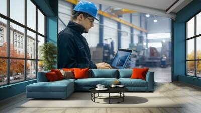 Factory worker in a hard hat is using a laptop computer with an engineering software. Wall mural