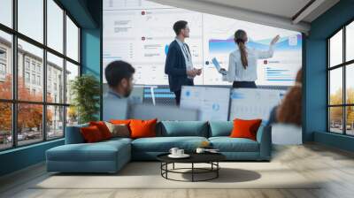 Female Data Scientist And Male Project Manager Discussing Reports And Graphs On Big Digital Screen In Monitoring Office. Diverse Employees Working Behind Computers in Artificial Intelligence Company. Wall mural