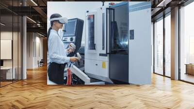 Female Engineer Wearing a Virtual Reality Headset and Operating a Heavy Industry Machine with Controllers at a Factory. Technician Configuring Industrial Machinery with the Help of VR Technology. Wall mural