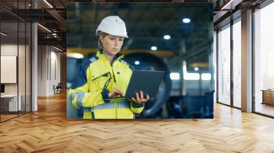 female industrial engineer in the hard hat uses laptop computer while standing in the heavy industry Wall mural