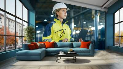 female industrial engineer in the hard hat uses laptop computer while standing in the heavy industry Wall mural