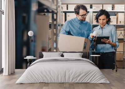 Female Inventory Manager Shows Digital Tablet Information to a Worker Holding Cardboard Box, They Talk and Do Work. In the Background Stock of Parcels with Products Ready for Shipment. Wall mural