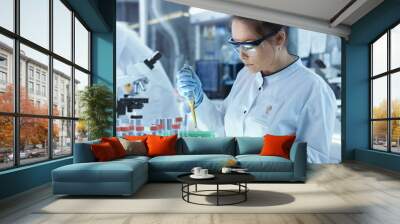 Female Research Scientist Uses Micropipette Filling Test Tubes in a Big Modern Laboratory. In the Background Scientists are Working. Wall mural