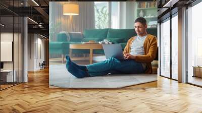 Handsome Adult Man Using Laptop Computer, while Sitting on Living Room Floor in Cozy Stylish Apartment. Attractive Man is Online Shopping on Internet, Watching Funny Videos on Streaming Service. Wall mural