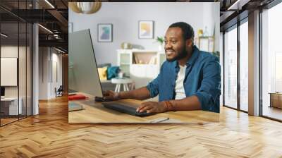 Handsome African Amertican Man Works on a Personal Computer while Sitting at the Desk of His Cozy Living Room. Wall mural