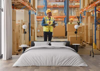 Handsome Male Worker Wearing Hard Hat Holding Digital Tablet Computer Walking Through Retail Warehouse full of Shelves with Goods. Working in Logistics and Distribution Center. Wall mural