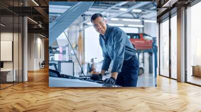 Handsome Professional Car Mechanic is Working on a Vehicle in a Service. Repairman Looks Happy While Using a Ratchet. Specialist is Wearing Safety Glasses. He Looks at a Camera and Smiles. Wall mural