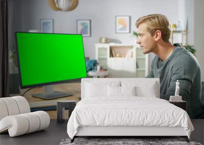 Handsome Young Man Works on a Green Mock-up Screen Personal Computer while Sitting at His Desk in the Cozy Apartment. Wall mural