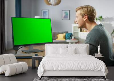 Handsome Young Man Works on a Green Mock-up Screen Personal Computer while Sitting at His Desk in the Cozy Apartment. Wall mural