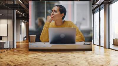 Happy Latin Marketing Specialist in Glasses Working on Laptop Computer in Busy Creative Office. Beautiful Diverse Female Project Manager Hesitating and Thinking Before Answering an Email to Colleague. Wall mural