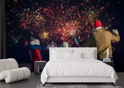 Happy New Year Celebration, Young Family of Three Standing in the Front Yard Watching Beautiful Fireworks. In the Evening while Snow is Falling Father, Mother and Cute Little Daughter Look up. Wall mural