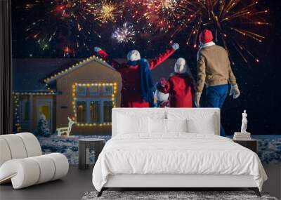 Happy New Year Celebration, Young Family of Three Standing in the Front Yard Watching Beautiful Fireworks. In the Evening while Snow is Falling Father, Mother and Cute Little Daughter Look up. Wall mural