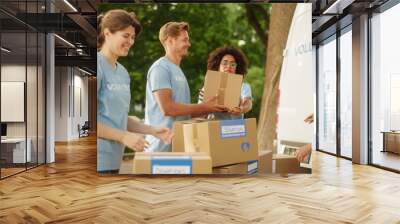 Happy Team of Young Volunteers Preparing Humanitarian Aid Rations, Food, Donations and Loading Cardboard Boxes in a Van on a Sunny Day. Charity Workers Work in Humanitarian Donation Center. Wall mural