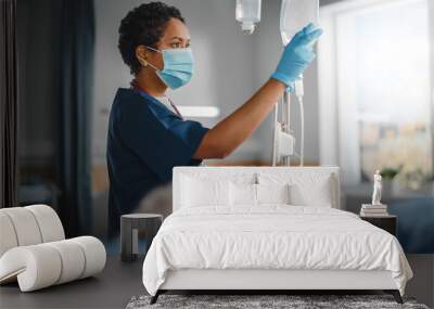 Hospital Ward: Professional Black Head Nurse Wearing Face Mask Does Checkup of Patient's Vitals, Checking Heart Rate Computer, Intravenous or Iv Fluids Drip Bag. Caring Nurse Monitors Person Recovery Wall mural