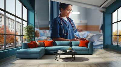 Hospital Ward: Professional Smiling Black Female Head Nurse or Doctor Wearing Stethoscope Uses Medical Computer. In the Background Patients in Beds Recovering Successfully after Sickness and Surgery Wall mural