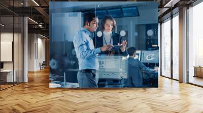 In Technology Research Facility: Female Project Manager Talks With Chief Engineer, they Consult Tablet Computer. Team of Industrial Engineers, Developers Work on Engine Design Using Computers Wall mural