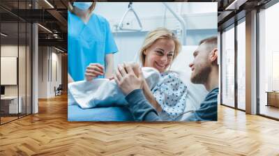 In the Hospital Midwife Gives Newborn Baby to a Mother to Hold, Supportive Father Lovingly Hugging Baby and Wife. Happy Family in the Modern Delivery Ward. Wall mural