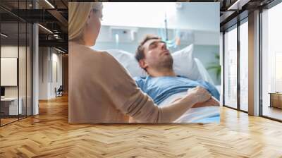 In the Hospital Sick Man Lying on the Bed, His Visiting Wife Hopefully Sits Beside Him Holds His Hands and Hopes for Recovery. Wall mural