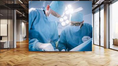 Low Angle Shot In Operating Room of Two Surgeons During the Surgery Procedure Bending Over Patient with Instruments. Professional Doctors in Modern Hospital Wall mural