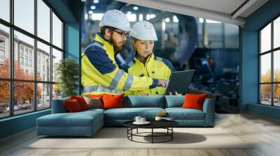 Male and Female Industrial Engineers in Hard Hats Discuss New Project while Using Laptop. They Make Showing Gestures.They Work in a Heavy Industry Manufacturing Factory. Wall mural