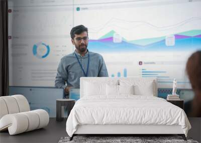 Male Indian Computer Scientist With Tablet Giving Presentation to Diverse Team Of Data Analysts In Front Of Big Digital Screen In Monitoring Room. Colleagues Listening To Training On Automation. Wall mural