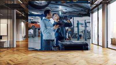 Manager Checks Data on a Tablet Computer and Explains the Breakdown to a Mechanic. Car Service Employees Inspect the Bottom of the Car with a LED Lamp. Modern Clean Workshop. Wall mural