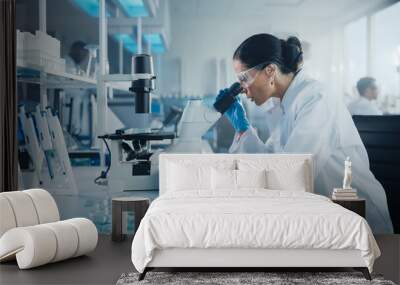 medical development laboratory: caucasian female scientist looking under microscope, analyzes petri  Wall mural