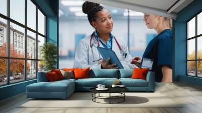 Medical Hospital: Professional Black Female Medical Doctor Talks with White Female Nurse Using Digital Tablet Computer. Two Health Care Specialists Discuss, Find Treatment Solution to Save Lives Wall mural