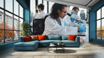 Medical Science Laboratory: Beautiful Black Scientist Looking Under Microscope Does Analysis of Test Sample. Diverse Team of Young Specialists, Using Advanced Technology Equipment. Wall mural