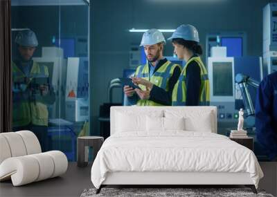 Modern Factory: Female and Male Engineers Wearing Safety Jackets, Hardhats Standing in Industrial Workshop, Talking and Using Tablet Computer. Facility with CNC Machinery, Robot Arm Production Line Wall mural