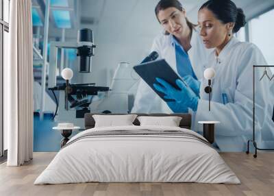 Modern Medical Research Laboratory: Two Female Scientists Working, Using Digital Tablet, Analysing Samples, Talking. Advanced Scientific Pharmaceutical Lab for Medicine, Biotechnology Development Wall mural