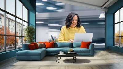 Modern Office: Happy Smiling Hispanic Businesswoman Sitting at Her Desk Working on a Laptop Computer Celebrates Victory. Latin Female Entrepreneur is a Happy Winner. Motion Blur Background Wall mural