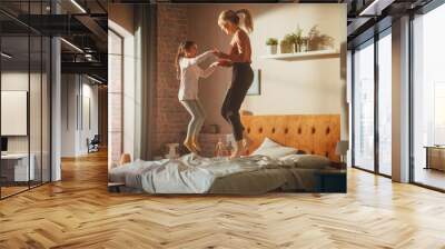 Mother and Small Daughter Having Fun at Home. Cheerfully Playing, Running Around and Jumping on a Bed in Stylish Loft Apartment. Happy Childhood, Parenthood and Motherhood Memories. Wall mural