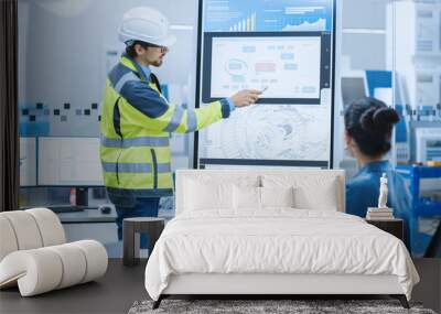 On a Meeting Chief Industrial Engineer Wearing Safety Jacket, and Hardhat Reports to a Group of Specialists, Managers, Uses Interactive Digital Whiteboard to Show New Eco Friendly Engine Technology Wall mural