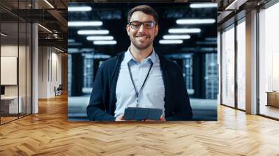 Portrait of a Bearded Handsome Caucasian IT Specialist in Glasses Standing with Tablet and Posing in the Middle of a Working Data Center Server Room with Server Computers Working on a Rack. Wall mural