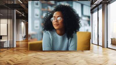 Portrait of a Beautiful Authentic Latina Female with Afro Hair Wearing Light Blue Jumper and Glasses. She Looks Away and Thinking about Life. Successful Woman Resting in Bright Living Room. Wall mural