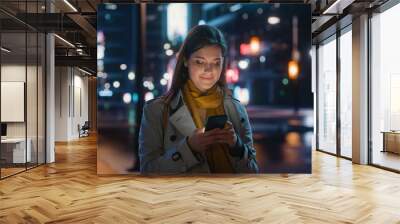 Portrait of a Beautiful Woman in Trench Coat Walking in a Modern City Street with Neon Lights at Night. Attractive Female Using Smartphone and Looking Around the Urban Cinematic Environment. Wall mural