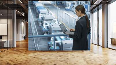 Portrait of a Caucasian Female Engineer Using Laptop Computer and Looking Around a Factory Facility with Robotic Arms Producing Modern Electronic Components for Tech Industries Wall mural