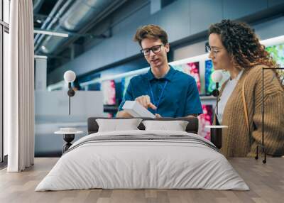 Portrait of a Female Customer Seeking Advice from Retail Home Electronics Expert. Hispanic Girl Explores Smartphone Options. Shopper Evaluating Latest Mobile Phone Innovations in a Department Store Wall mural