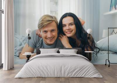 Portrait of a Happy Young Family Having Fun in Bed on a Lazy Sunday Afternoon. Attractive Young People Looking at Camera Smiling Happily Wall mural