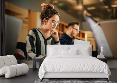 Portrait of Enthusiastic Hispanic Young Woman Working on Computer in a Modern Bright Office. Confident Human Resources Agent Smiling Happily While Collaborating Online with Colleagues. Wall mural