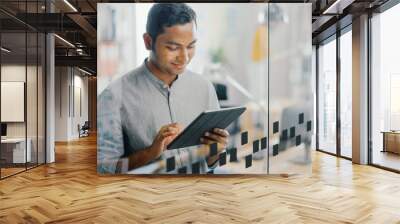 Portrait of Handsome Professional Indian Man Uses Touch Screen Digital Tablet Computer, Writes Important Email, Smiles Charmingly. Successful Man Working in Bright Diverse Office. Wall mural