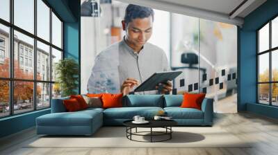 Portrait of Handsome Professional Indian Man Uses Touch Screen Digital Tablet Computer, Writes Important Email, Smiles Charmingly. Successful Man Working in Bright Diverse Office. Wall mural