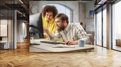 Portrait of Two Creative Colleagues Collaborating and Pointing at the Computer Screen in Modern Bright Office. Biracial Young Woman Discussing Work with Caucasian Male Assistant. Wall mural