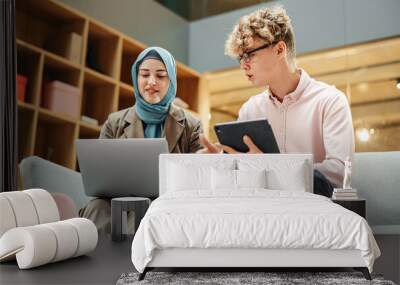 Portrait of Two Creative Colleagues Collaborating and Working with the Laptop in Modern Office. Muslim Female Manager Consults White Project Manager, They Brainstorm on the Project Wall mural