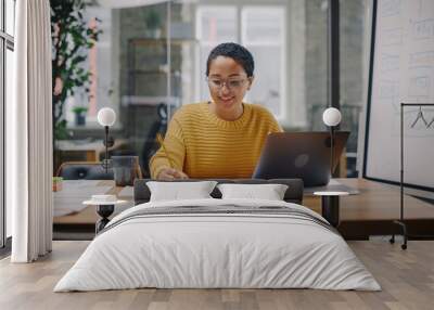 Portrait of Young Latin Marketing Specialist in Glasses Working on Laptop Computer in Busy Creative Office Environment. Beautiful Diverse Multiethnic Female Project Manager is Browsing Internet. Wall mural